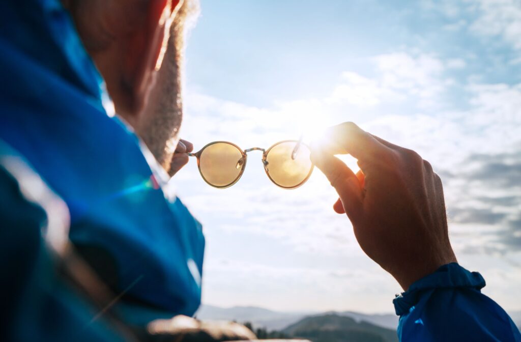 A person holding polarized sunglasses up to the sunlight, highlighting glare reduction features.