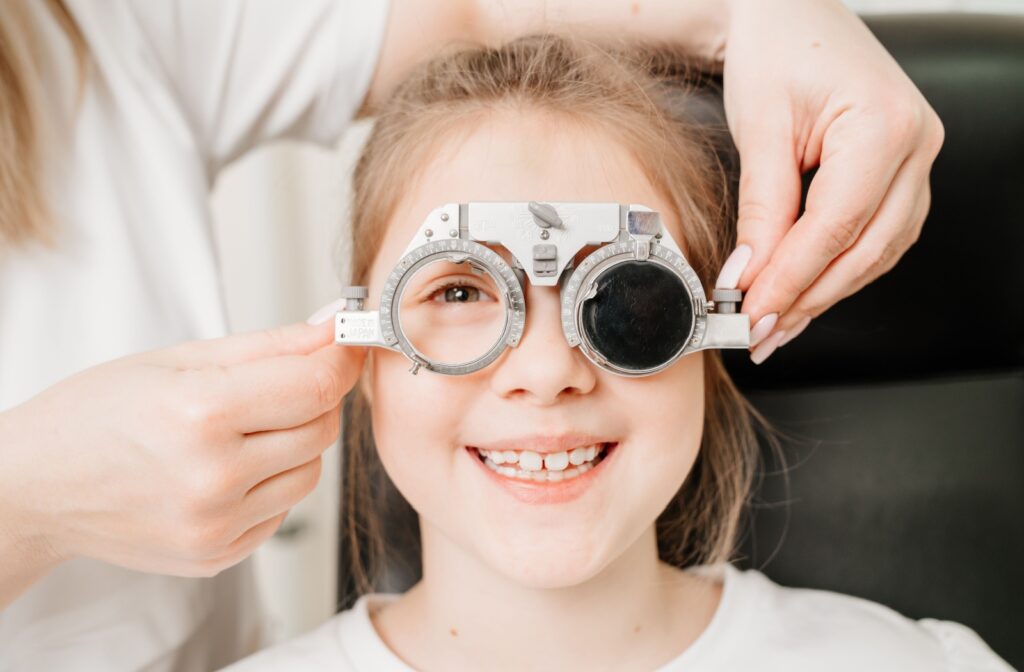 A smiling child gets an eye exam from an optometrist.