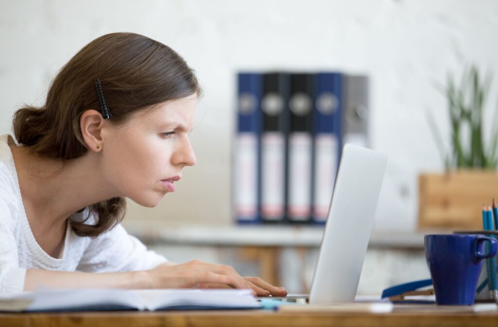 A person leans forward and squints at her laptop screen, showing she’s having trouble seeing clearly.