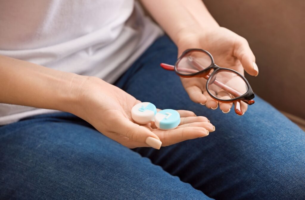Close-up of a seated person holding glasses in one hand and a contact lens case in the other.