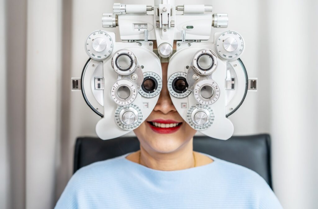 A smiling older adult behind a phoropter: a large mask-like device with knobs and lenses.