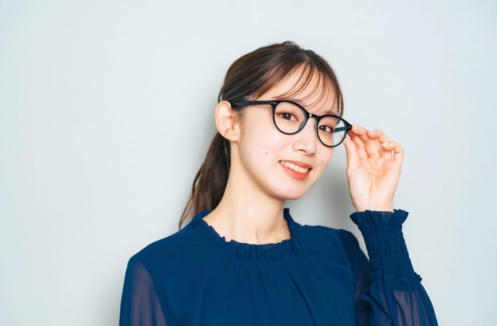 A young women wearing a blue top adjusts her glasses on her face